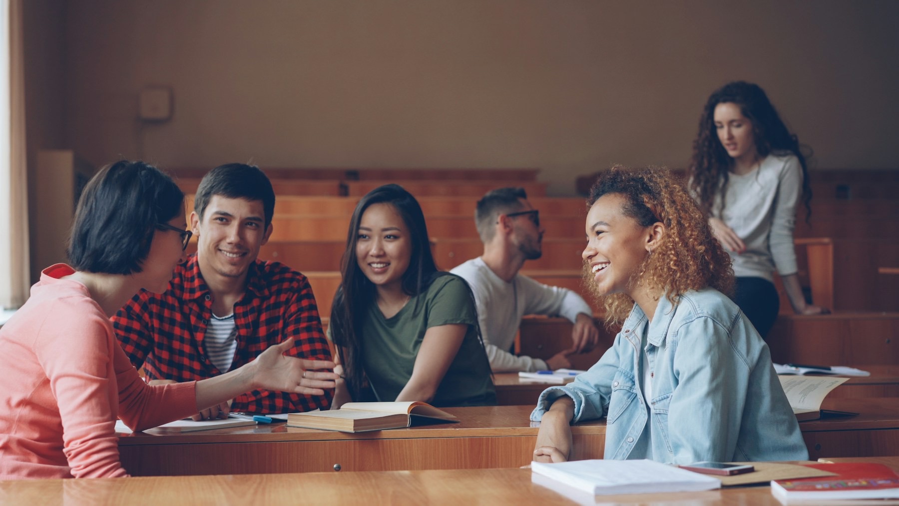 University students sitting at lecture-hall desks, talking and laughing together